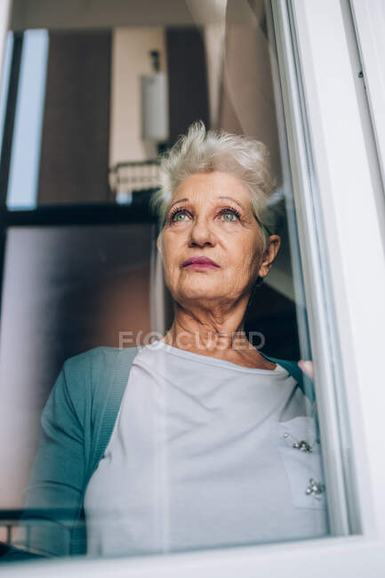 Vue de la femme âgée par la fenêtre — Photo de stock
