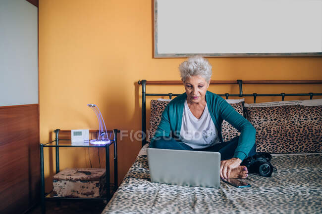 Fotógrafo sentado en la cama con portátil - foto de stock