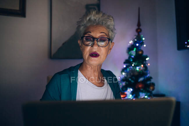 Mulher usando laptop à noite, árvore de Natal no fundo — Fotografia de Stock