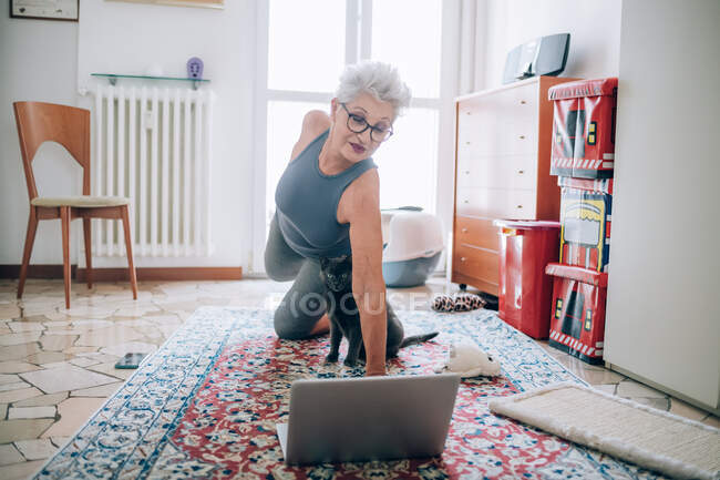 Mujer siguiendo en línea clases de yoga con su gato - foto de stock