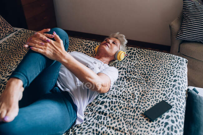 Frau entspannt sich im Bett, hört Kopfhörer und dehnt sich — Stockfoto