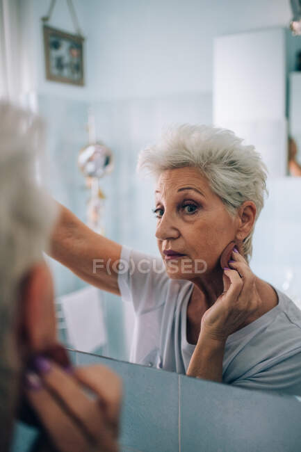 Donna anziana guardando allo specchio, applicando il trucco — Foto stock