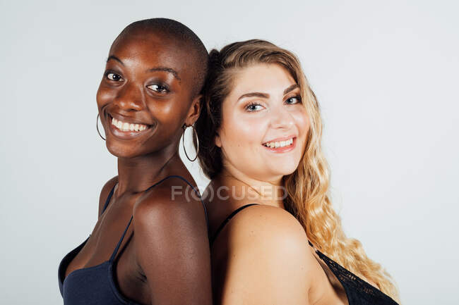 Dos mujeres jóvenes sonriendo, espalda con espalda - foto de stock