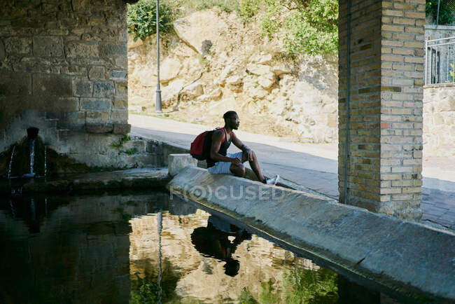 Молодий чоловік сидить біля води, роблячи перерву на прогулянці — стокове фото