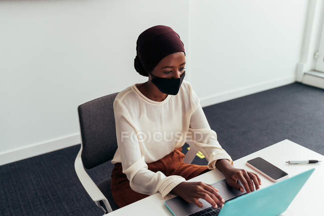 Donna che lavora sul computer portatile, indossando maschera — Foto stock