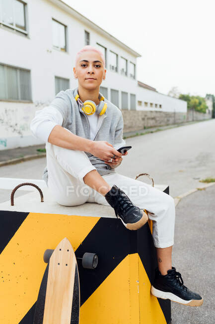 Молода жінка сидить перед будівлями, тримаючи мобільний телефон — стокове фото