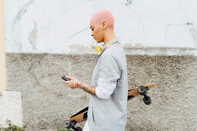 Vue latérale du skateboarder en utilisant un téléphone portable — Photo de stock