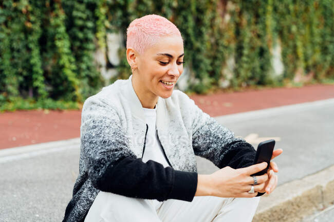 Молодая женщина сидит на тротуаре, используя мобильный телефон — стоковое фото