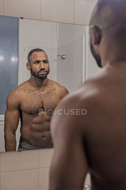 Homme poitrine nue se regardant dans le miroir de salle de bains — Photo de stock