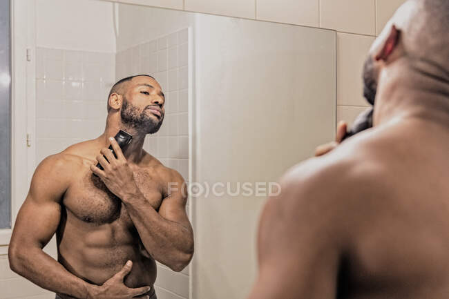 Hombre afeitándose con maquinilla de afeitar eléctrica, mirando en el espejo - foto de stock