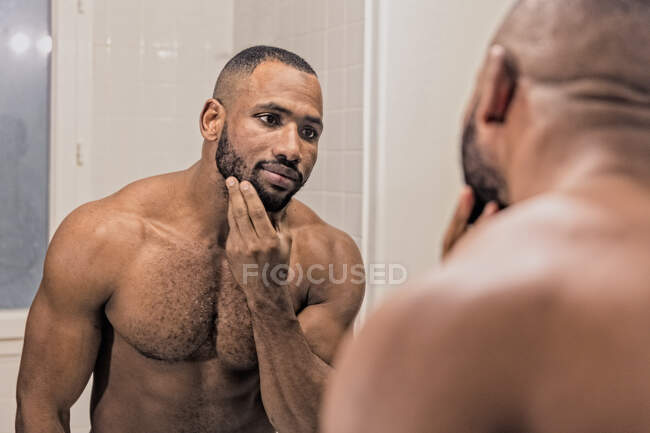 Чоловік дивиться у дзеркало, торкаючись бороди — стокове фото
