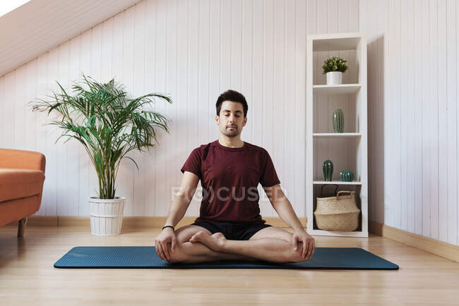 Mann meditiert zu Hause, sitzt mit gekreuzten Beinen — Stockfoto
