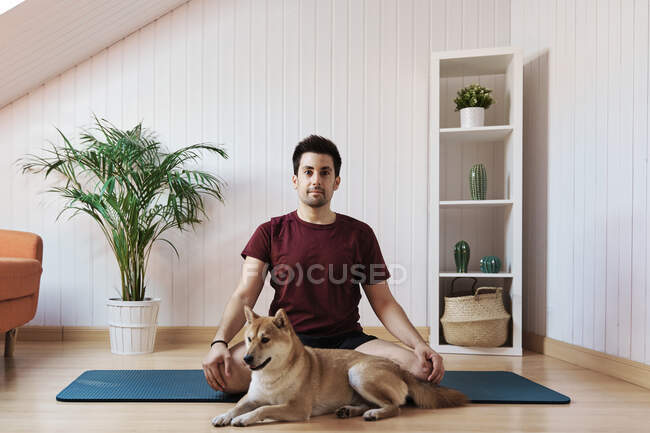 Hombre sentado en alfombra de ejercicio con perro mascota - foto de stock