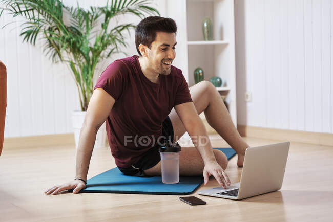 Uomo sul tappeto esercizio a casa, utilizzando il computer portatile — Foto stock