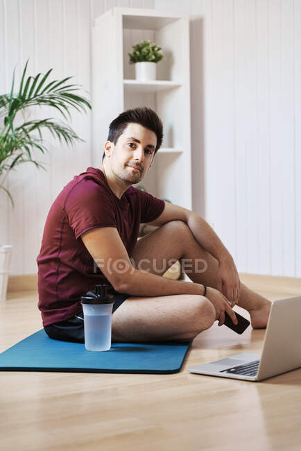 Hombre en casa con alfombra de ejercicio y portátil - foto de stock