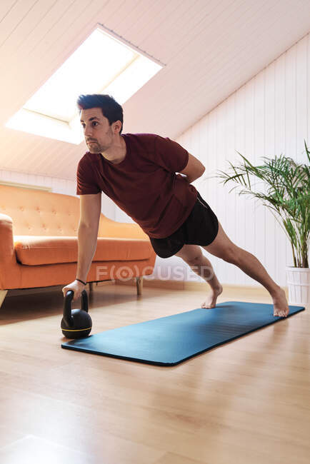 Мужчина тренируется дома, используя гири — стоковое фото