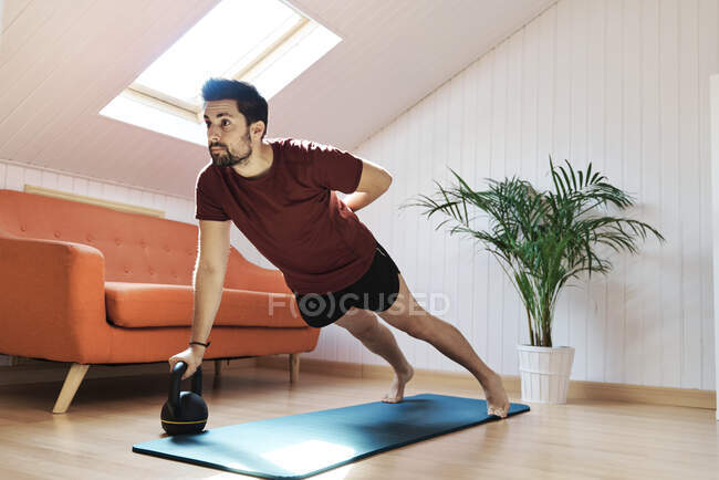 Hombre haciendo ejercicio en casa, empujando hacia arriba con kettlebell - foto de stock