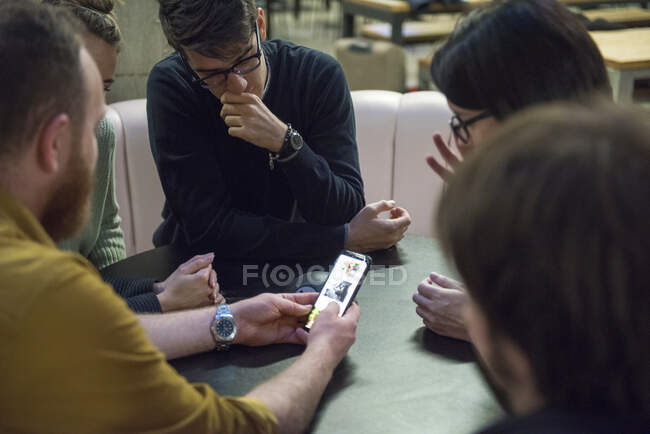 Студенты сидят вместе, смотрят на смартфон — стоковое фото