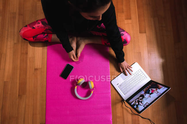 Giovane donna seduta su stuoia di yoga, avendo videochiamata sul computer portatile — Foto stock
