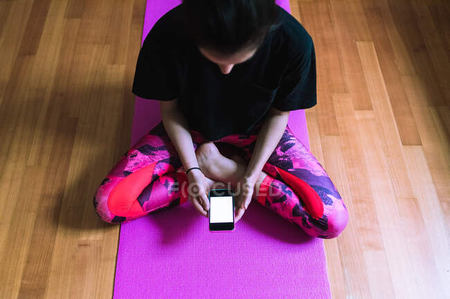 Young woman sitting on yoga mat with mobile phone — Stock Photo