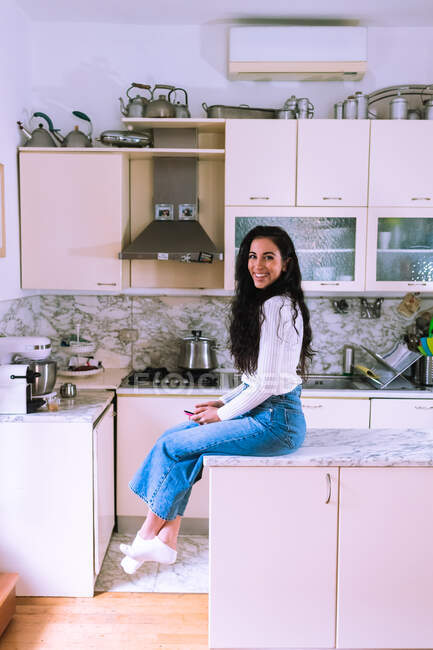Jovem mulher sentada no balcão da cozinha — Fotografia de Stock