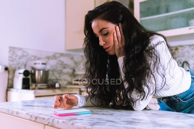 Молода жінка дивиться на свій телефон на кухні — стокове фото