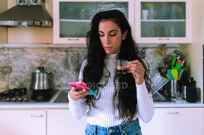 Junge Frau trinkt Kaffee und schaut auf ihr Handy — Stockfoto