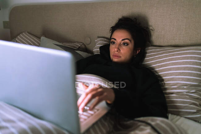 Jeune femme travaillant sur ordinateur portable au lit — Photo de stock