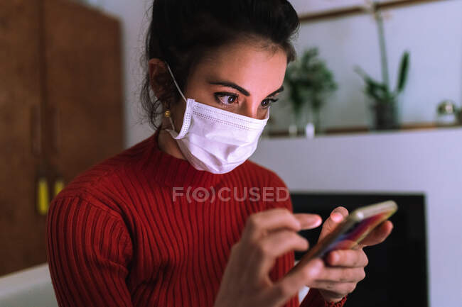 Jovem mulher usando máscara coronavírus, olhando para o telefone — Fotografia de Stock