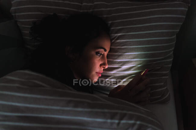 Jeune femme couchée au lit et regardant le téléphone — Photo de stock