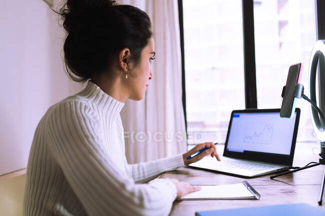 Jeune femme travaillant de la maison avec ordinateur portable, téléphone et anneau lumineux — Photo de stock