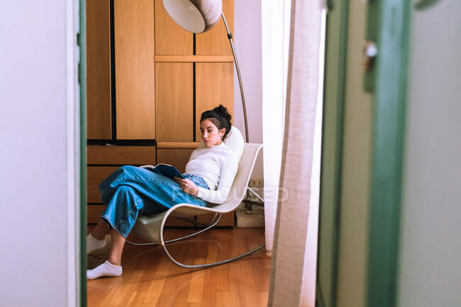 Jovem mulher sentada em uma cadeira e lendo — Fotografia de Stock