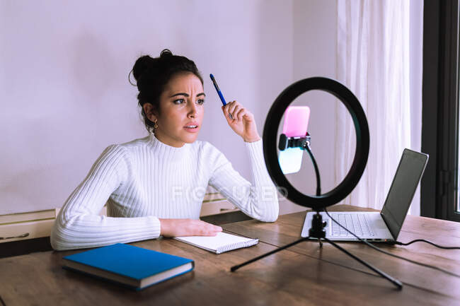 Mujer joven que trabaja desde casa con portátil, teléfono y luz de timbre - foto de stock