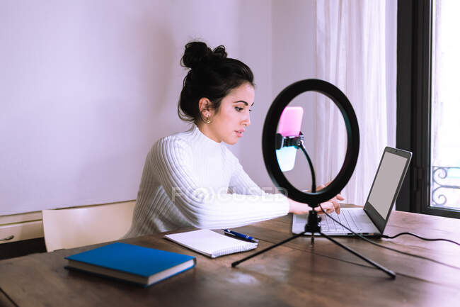Jovem mulher trabalhando em casa com laptop, telefone e anel de luz — Fotografia de Stock