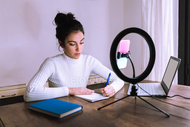 Young woman working from home with laptop, phone and ring light — Stock Photo