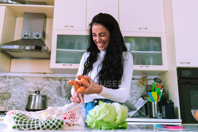 Mujer joven desempacando comestibles y riendo - foto de stock