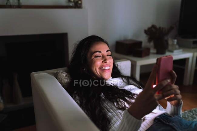 Jovem no sofá, sorrindo para o telefone celular — Fotografia de Stock