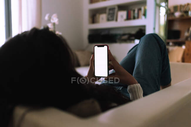 Молодая женщина на диване, смотрит на мобильный телефон — стоковое фото