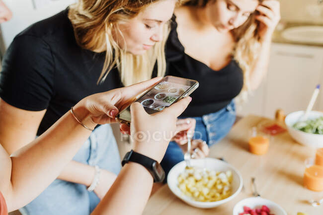 Frau fotografiert am Telefon, wie Freunde Essen zubereiten — Stockfoto