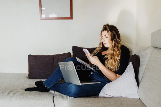 Junge Frau nutzt Smartphone und Laptop zu Hause — Stockfoto