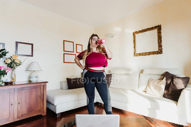 Mujer joven bebiendo agua durante la clase de ejercicio en línea - foto de stock