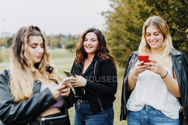 Três jovens mulheres usando seus telefones no parque — Fotografia de Stock