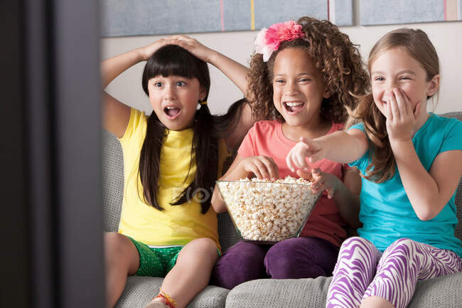 Três meninas assistindo tv comer pipocas — Fotografia de Stock