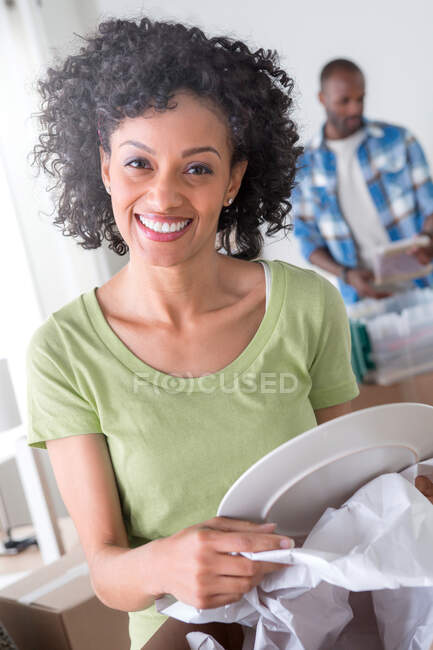 Mid adult woman unwrapping plate, man in background — Stock Photo