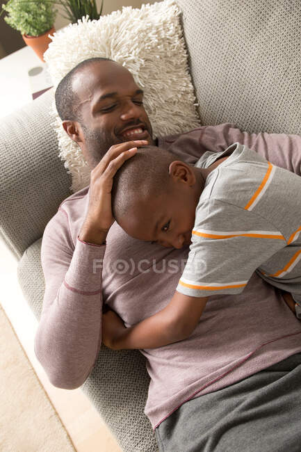 Padre e hijo tumbados en el sofá - foto de stock