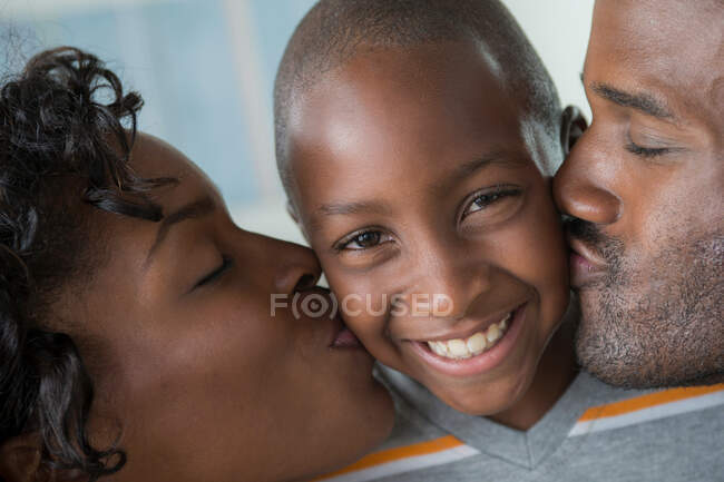 Madre y padre besar hijo en las mejillas - foto de stock