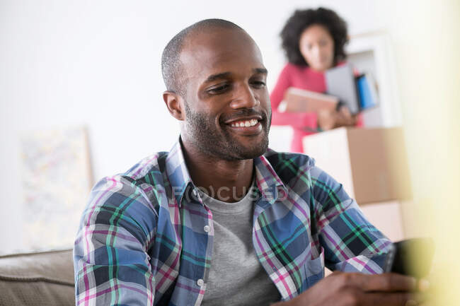 Mittlerer erwachsener Mann mit Handy, Frau im Hintergrund — Stockfoto