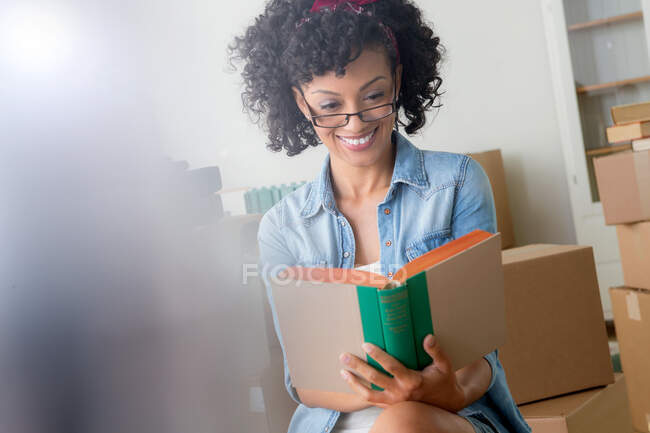 Mulher adulta média leitura livro cercado por caixas de papelão — Fotografia de Stock