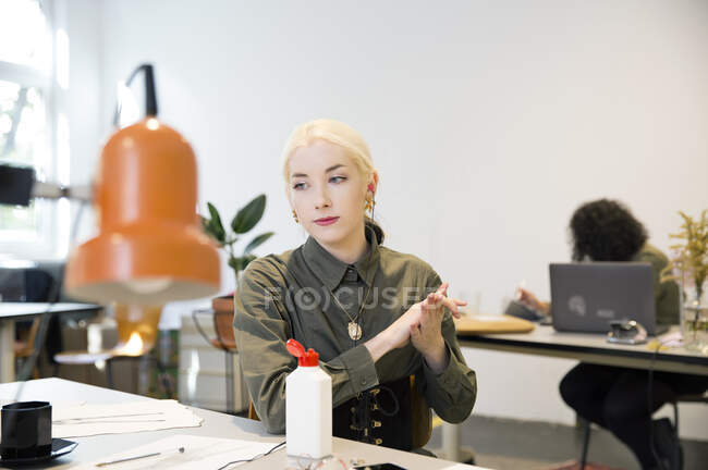 Молода жінка використовує дезінфікуючий засіб для рук за її столом — стокове фото