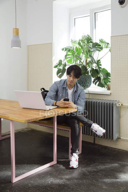 Молодой человек с телефоном и ноутбуком в коворкинге — стоковое фото
